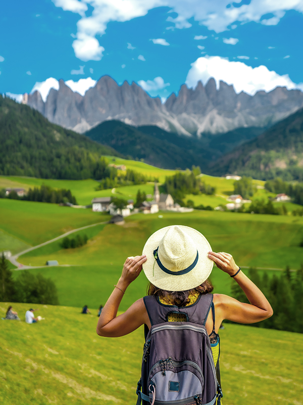 Tourist holding her hat while admiring the dolomites landscape in summer